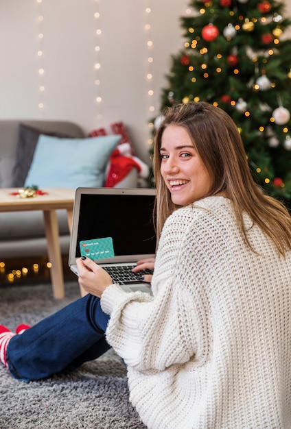 Mujer joven sonriente con tarjeta de crédito y computadora portátil