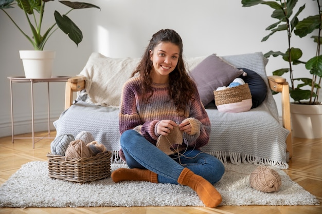 Mujer joven sonriente de tiro completo tejiendo