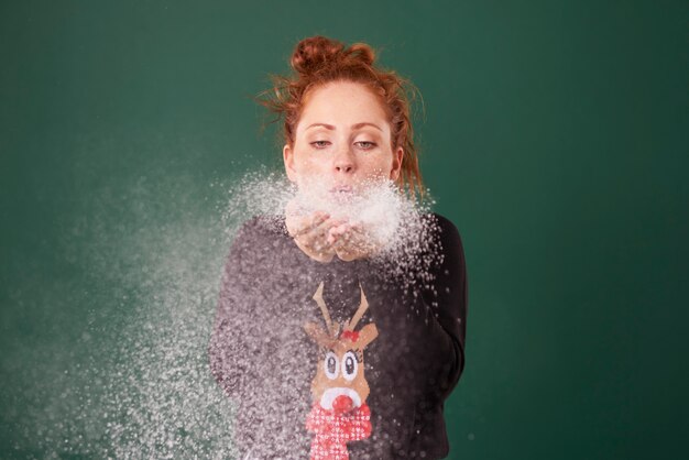 Mujer joven soplando nieve falsa