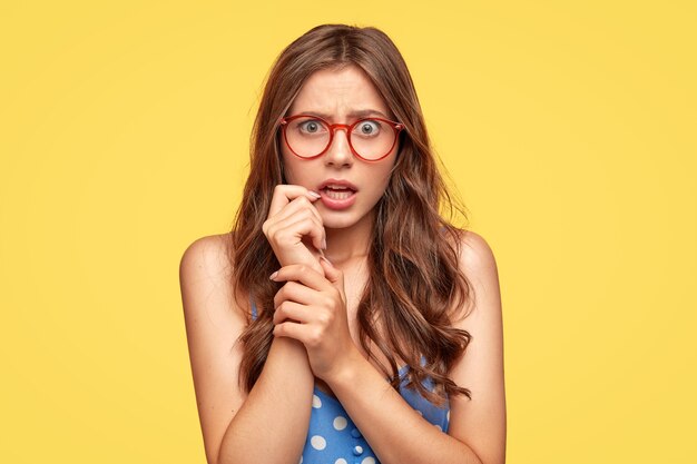 Mujer joven sorprendida disgustada con gafas posando contra la pared amarilla