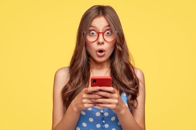 Foto gratuita mujer joven sorprendida con gafas posando contra la pared amarilla