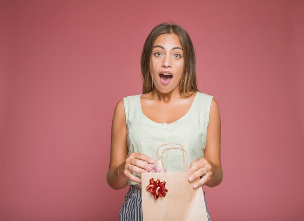 Mujer joven sorprendida que sostiene la caja de regalo del bolso de compras de papel