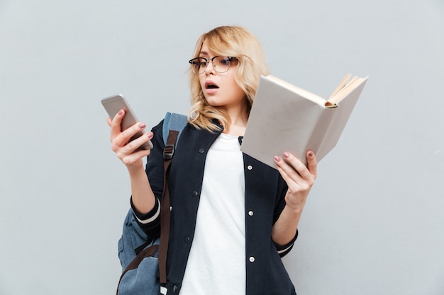 Mujer joven sorprendida que usa el teléfono y sosteniendo el libro.