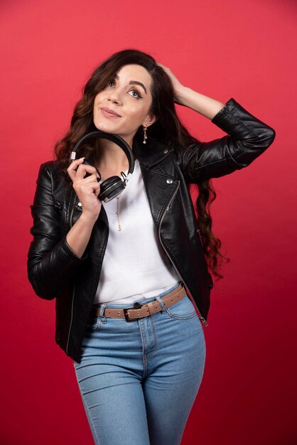 Mujer joven sosteniendo auriculares y posando sobre un fondo rojo. Foto de alta calidad