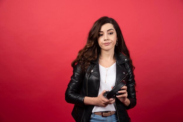 Mujer joven sosteniendo auriculares y posando sobre un fondo rojo. Foto de alta calidad