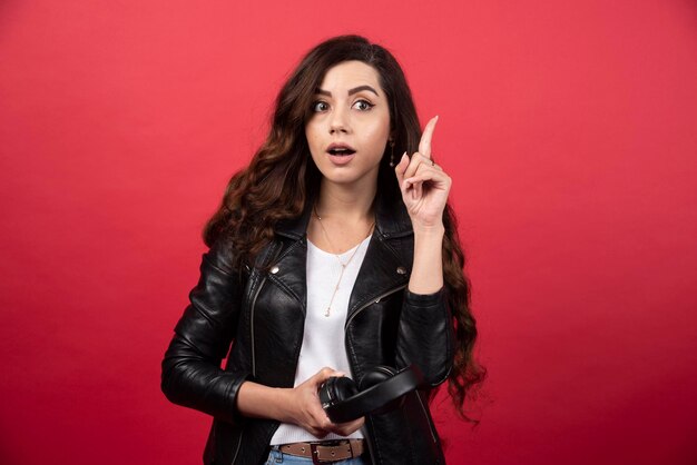 Mujer joven sosteniendo auriculares y posando sobre un fondo rojo. Foto de alta calidad