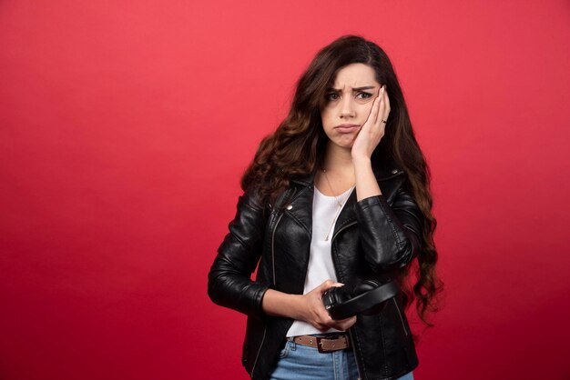 Mujer joven sosteniendo auriculares y posando sobre un fondo rojo. Foto de alta calidad