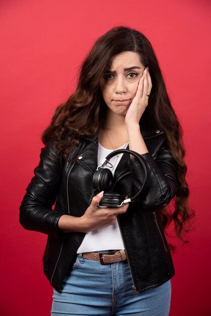 Mujer joven sosteniendo auriculares y posando sobre un fondo rojo. Foto de alta calidad