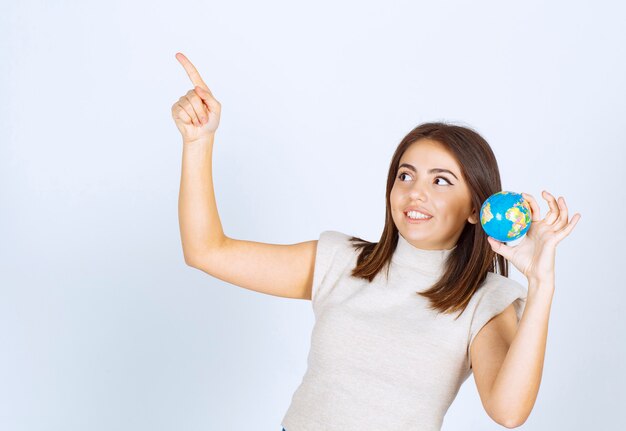 Mujer joven sosteniendo una bola de globo terráqueo y apuntando hacia arriba con un dedo índice