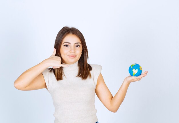 Mujer joven sosteniendo una bola de globo terráqueo y haciendo una señal de llamada telefónica