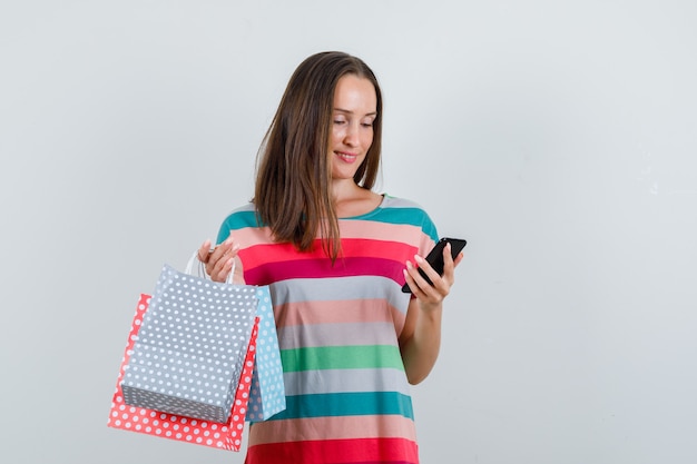 Foto gratuita mujer joven sosteniendo bolsas de papel y mirando el teléfono en la vista frontal de la camiseta.