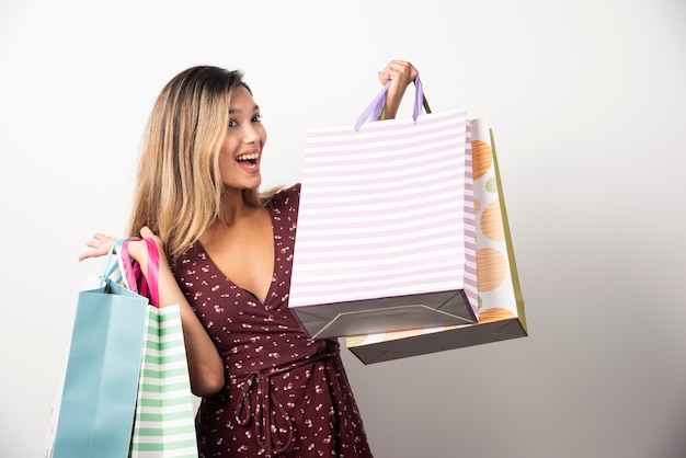 Mujer joven sosteniendo bolsas de la tienda en la pared blanca.