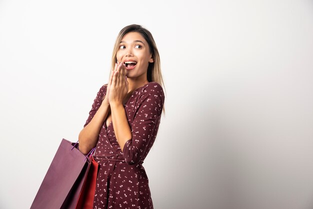 Mujer joven sosteniendo bolsas de la tienda en la pared blanca.