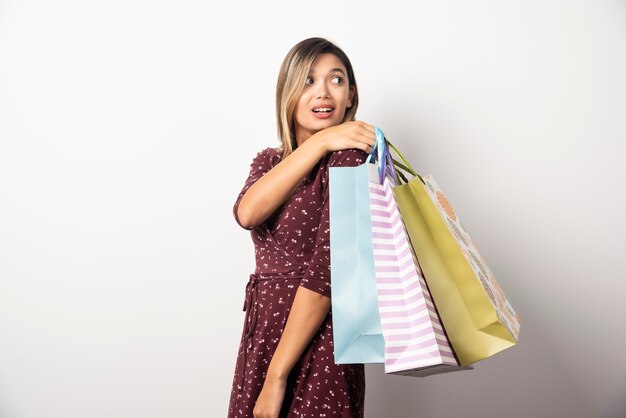 Mujer joven sosteniendo bolsas de la tienda en la pared blanca.