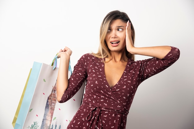 Mujer joven sosteniendo bolsas de la tienda en la pared blanca.