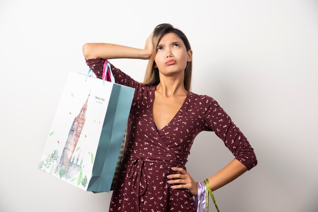 Mujer joven sosteniendo bolsas de la tienda en la pared blanca.