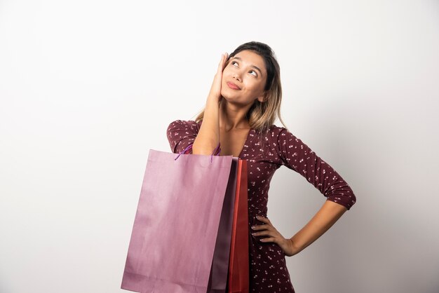 Mujer joven sosteniendo bolsas de la tienda en la pared blanca.