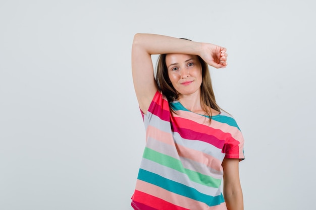 Foto gratuita mujer joven sosteniendo el brazo levantado en la frente en camiseta y mirando alegre, vista frontal.