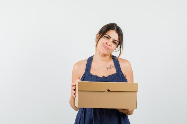 Mujer joven sosteniendo una caja de cartón en vestido y mirando confiado