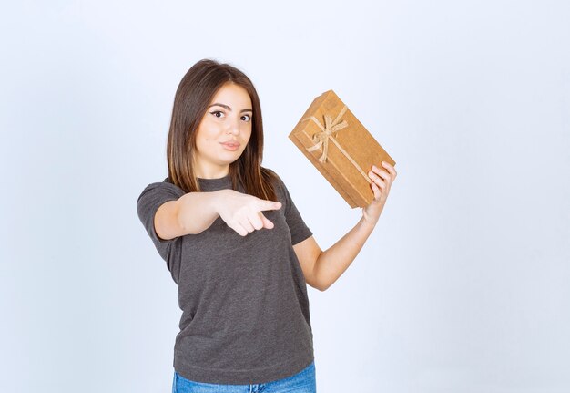 mujer joven sosteniendo una caja de regalo y apuntando a la cámara.