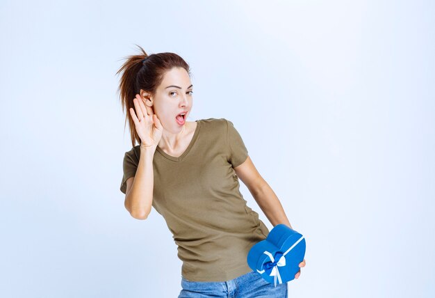 Mujer joven sosteniendo una caja de regalo azul con forma de oído y sintiéndose satisfecho