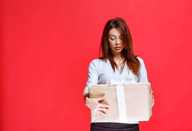 Mujer joven sosteniendo una caja de regalo de cartón y parece confundida y pensativa