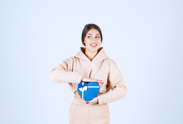 Mujer joven sosteniendo una caja de regalo con forma de corazón azul y parece feliz