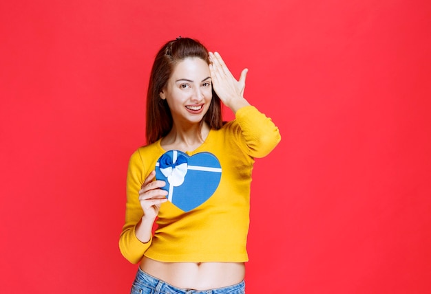 Mujer joven sosteniendo una caja de regalo con forma de corazón azul, sintiéndose positivo y feliz