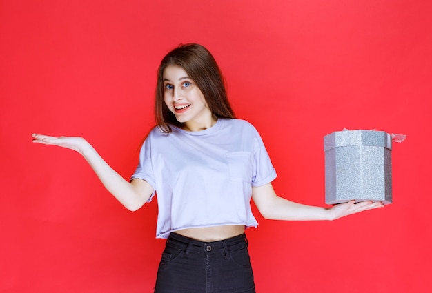 mujer joven sosteniendo una caja de regalo plateada y sintiéndose feliz.