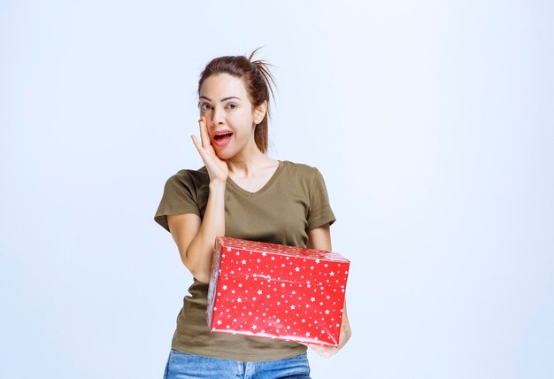 Mujer joven sosteniendo una caja de regalo roja y disfrutándola mucho