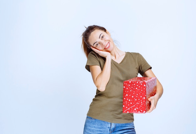 Mujer joven sosteniendo una caja de regalo roja y disfrutándola mucho