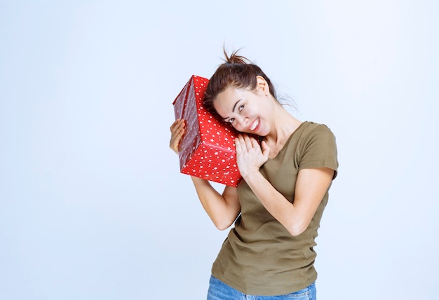 Mujer joven sosteniendo una caja de regalo roja por encima y por encima de su cabeza