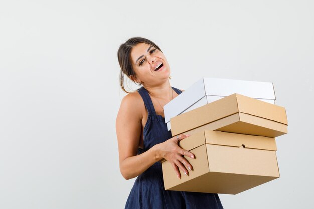 Mujer joven sosteniendo cajas de cartón en vestido y mirando alegre