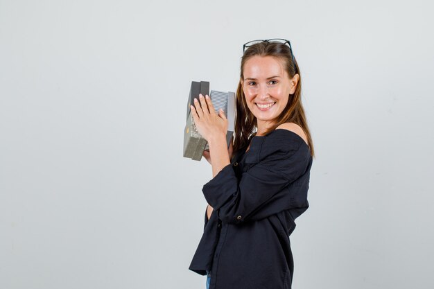 Mujer joven sosteniendo cajas de regalo en camisa, pantalones cortos, gafas y mirando alegre. .