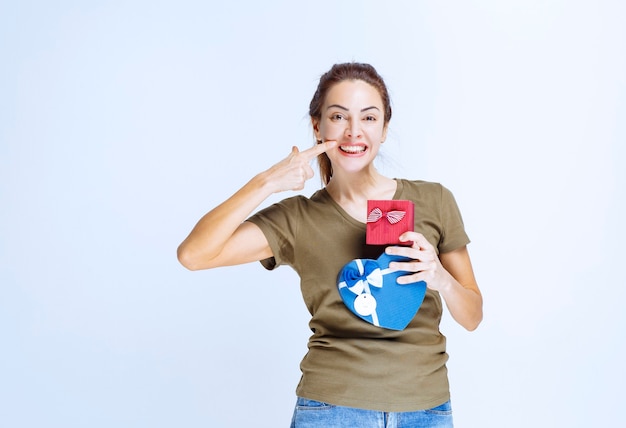 Mujer joven sosteniendo cajas de regalo rojas y azules con forma de corazón y disfrutándolas