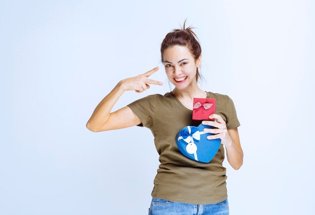 Mujer joven sosteniendo cajas de regalo rojas y azules con forma de corazón y disfrutándolas