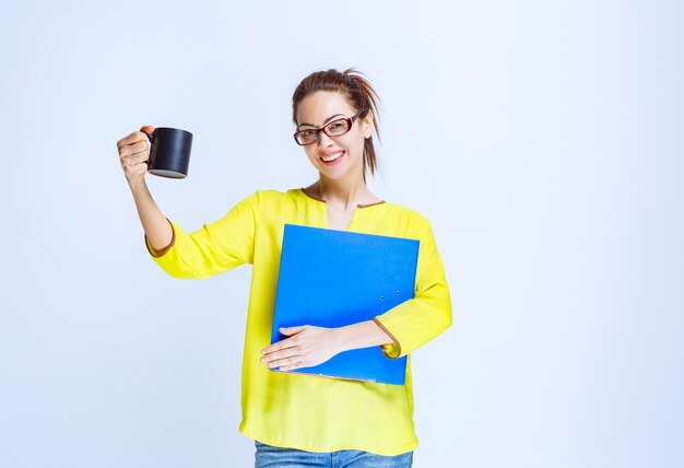 Mujer joven sosteniendo una carpeta azul y una taza de bebida negra