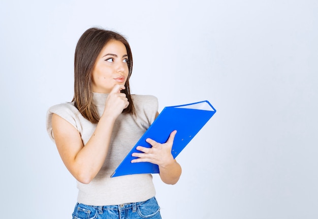 Mujer joven sosteniendo una carpeta y pensando.