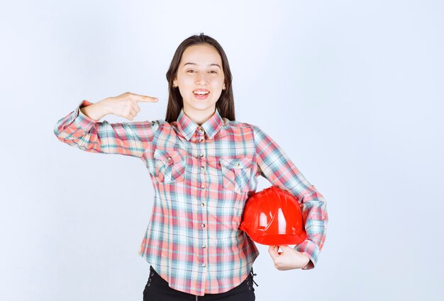 Una mujer joven sosteniendo un casco rojo y apuntando a un lado con el dedo.