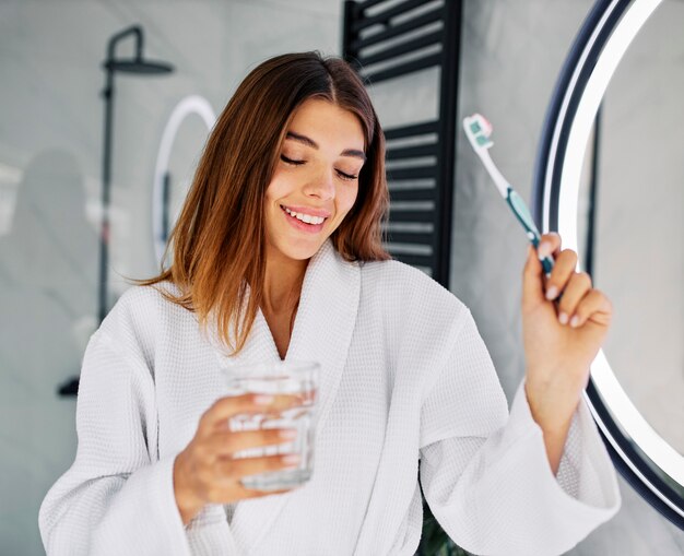 Mujer joven sosteniendo un cepillo de dientes y un vaso de agua