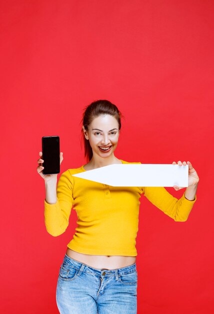 Mujer joven sosteniendo una flecha apuntando hacia la izquierda y un teléfono inteligente negro