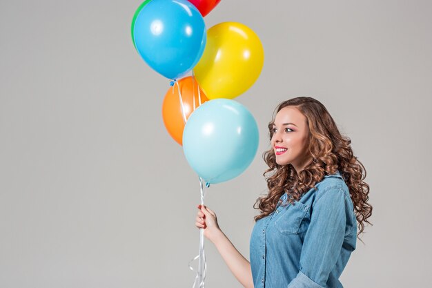 Mujer joven sosteniendo globos de colores en la pared gris del estudio