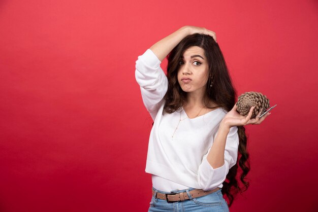 Mujer joven sosteniendo una gran piña de Navidad sobre fondo rojo. Foto de alta calidad