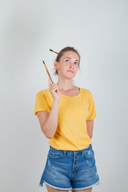 Mujer joven sosteniendo un lápiz y mirando hacia arriba en camiseta amarilla