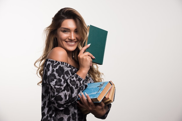 Foto gratuita mujer joven sosteniendo libros mientras se ríe en la pared blanca.