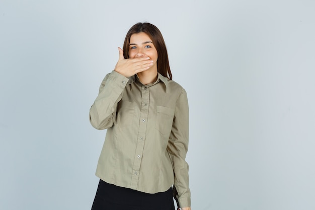 Mujer joven sosteniendo la mano en la boca en camisa y mirando feliz
