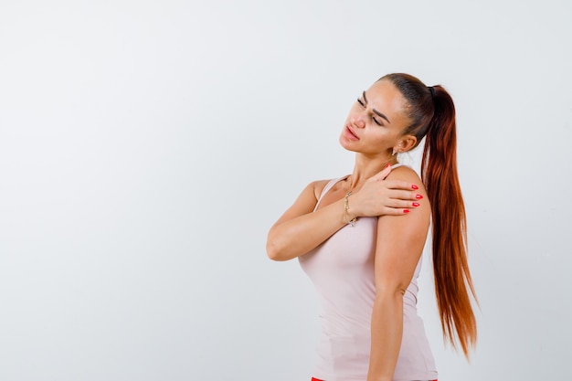 Foto gratuita mujer joven sosteniendo la mano en el brazo en la camiseta blanca y mirando pensativo, vista frontal.