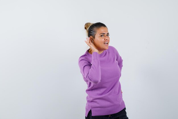 Mujer joven sosteniendo la mano cerca de la oreja para escuchar algo