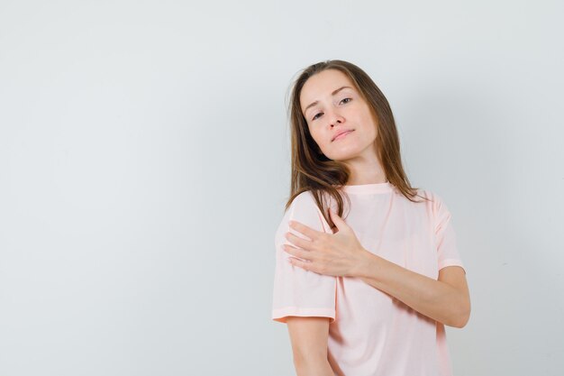 Mujer joven sosteniendo la mano en el otro brazo en camiseta rosa y mirando confiado.