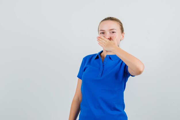 Mujer joven sosteniendo la mano sobre la boca en camiseta azul